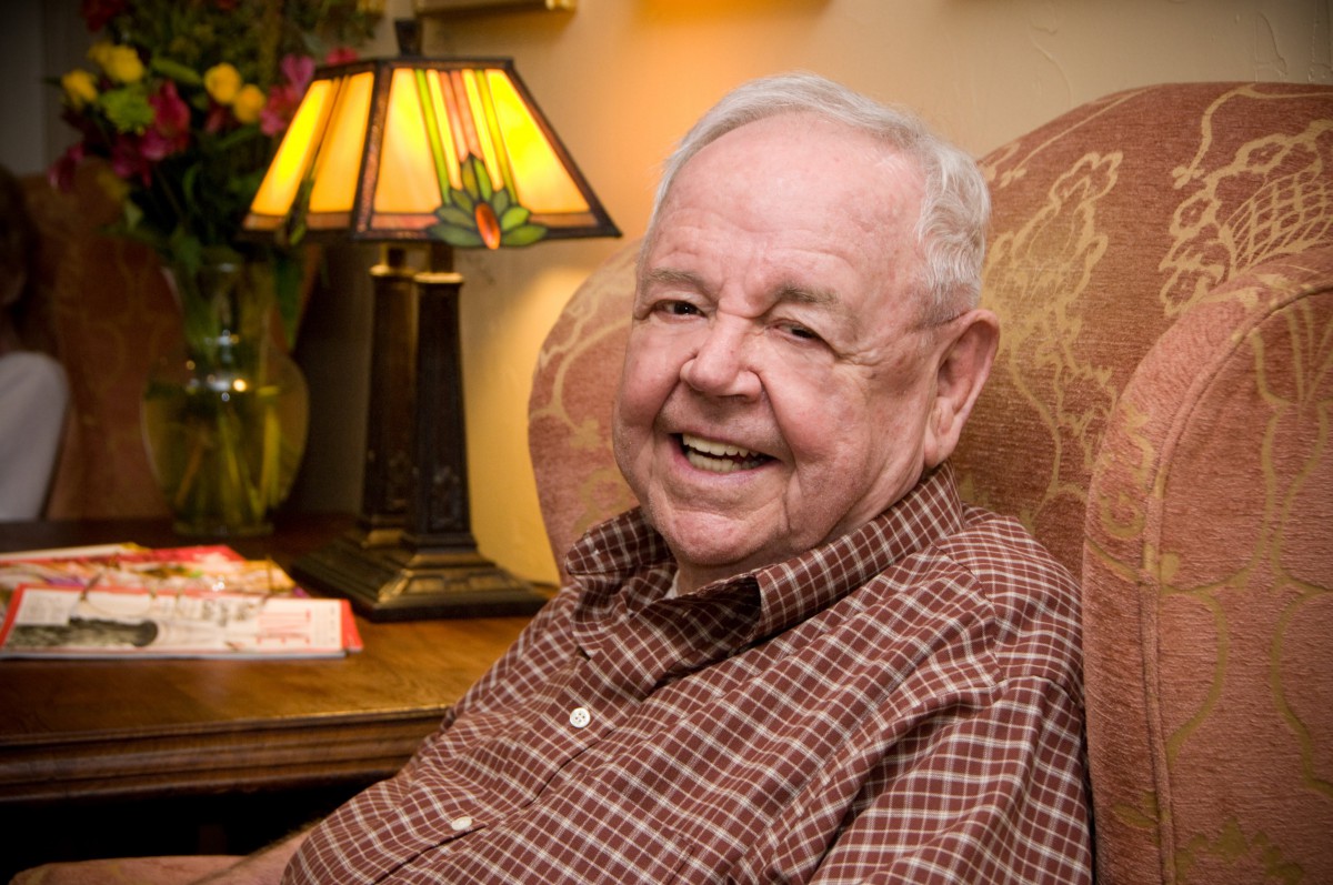 An elderly man sitting in a chair and smiling indoors.