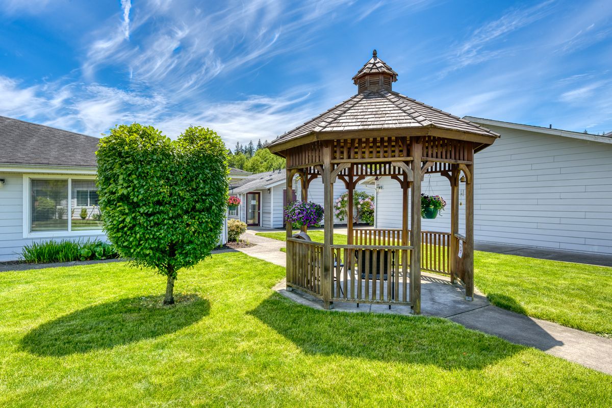 A wooden gazebo in a well-maintained garden on a sunny day.
