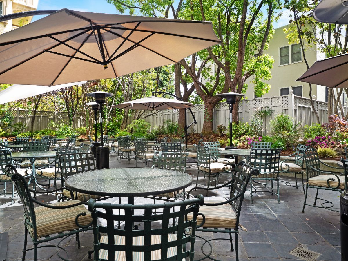 A cozy outdoor patio with tables, chairs, and large umbrellas set amidst a garden environment.