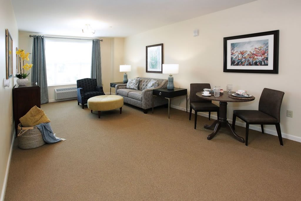 A spacious living room with a sofa, chairs, and tables, featuring carpeted flooring and elegant decor.