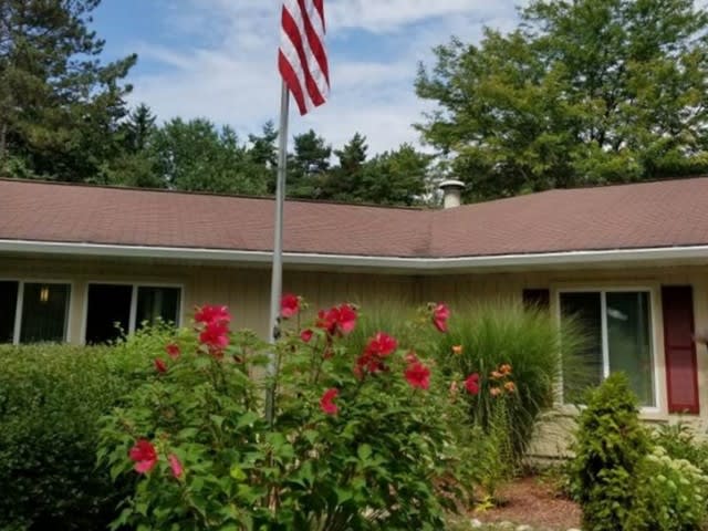 A suburban house with a well-maintained garden featuring red flowers and an American flag in front.