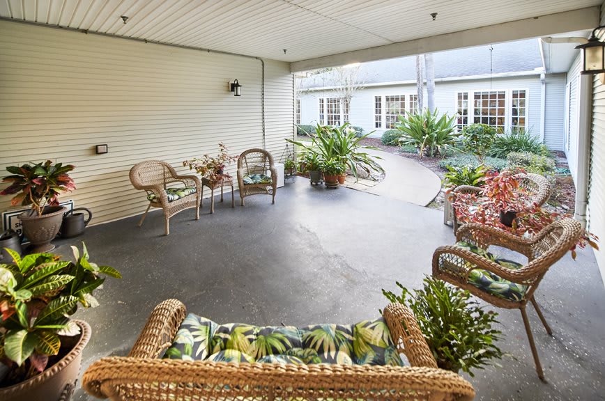 A cozy covered patio area with wicker furniture and lush greenery.