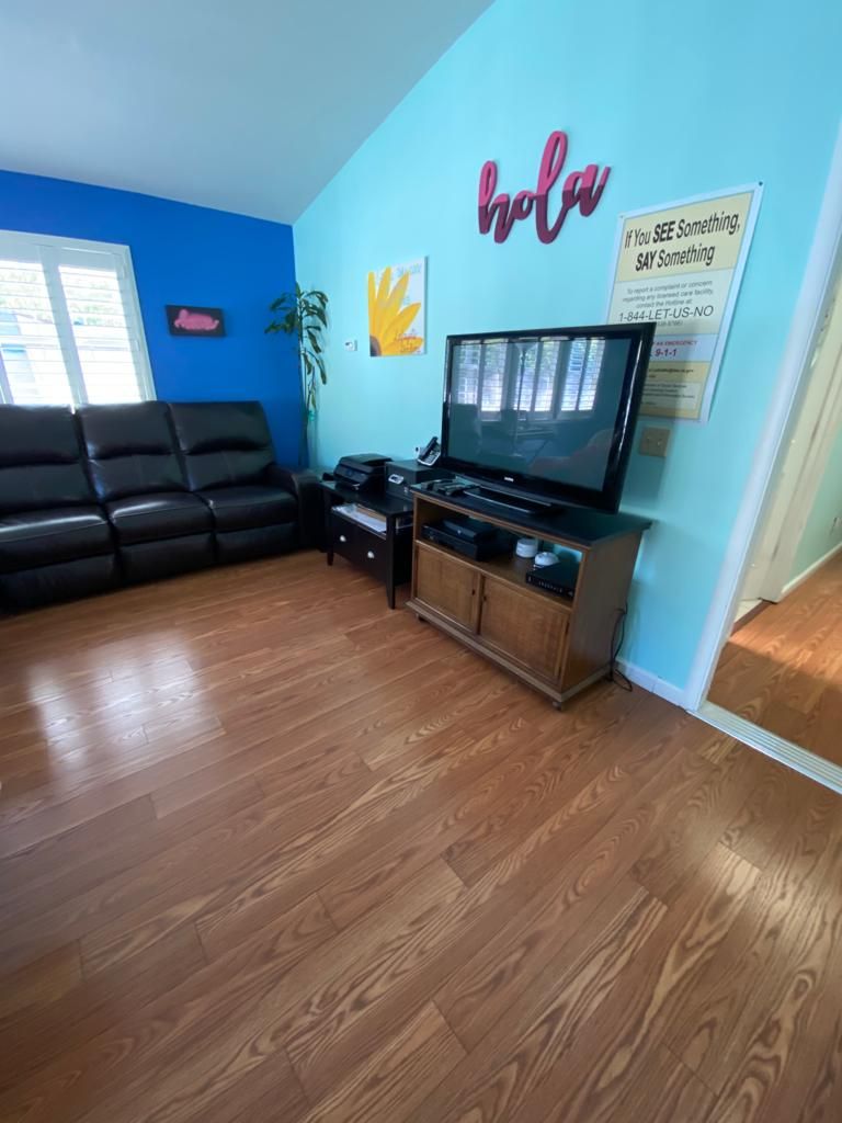 A cozy living room with a television, leather couch, and colorful wall decor.