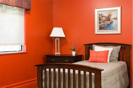 A modern bedroom featuring vibrant orange walls, a cozy bed adorned with pillows, and a stylish lamp.