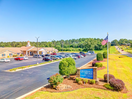 A scenic view of a building with a spacious parking lot, surrounded by greenery under a clear blue sky.
