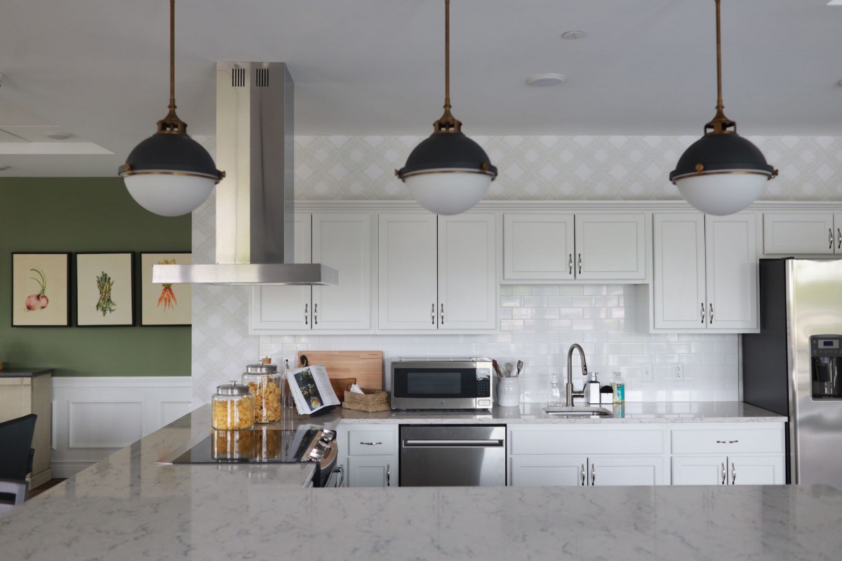 A modern kitchen with white cabinets, pendant lights, and stainless steel appliances.