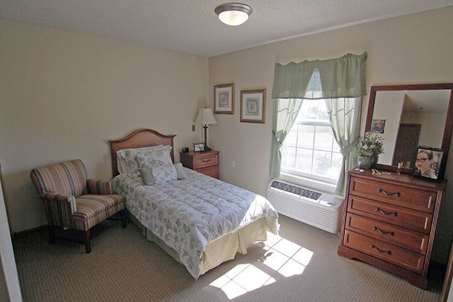 A cozy bedroom with a single bed, wooden furniture, and a window letting in natural light.