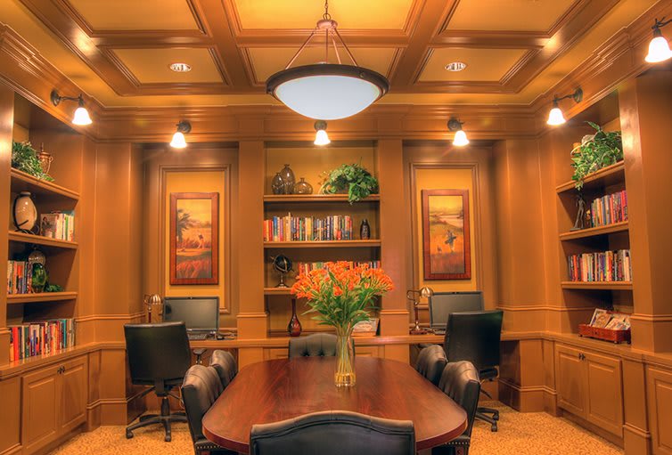 A luxurious conference room with wood paneling, a large meeting table, and comfortable chairs, adorned with artwork and a bookshelf.
