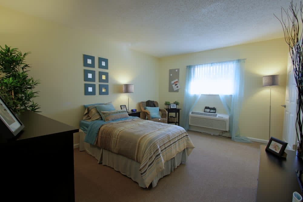 A cozy bedroom with light-colored walls and furnishings, featuring a bed, side tables, and a window.