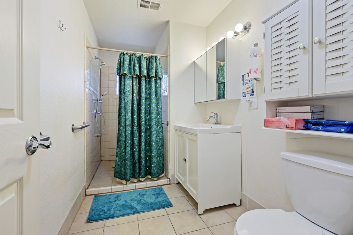 A clean bathroom with a shower, sink, and mirror, featuring teal curtains and a bath mat on the tile floor.