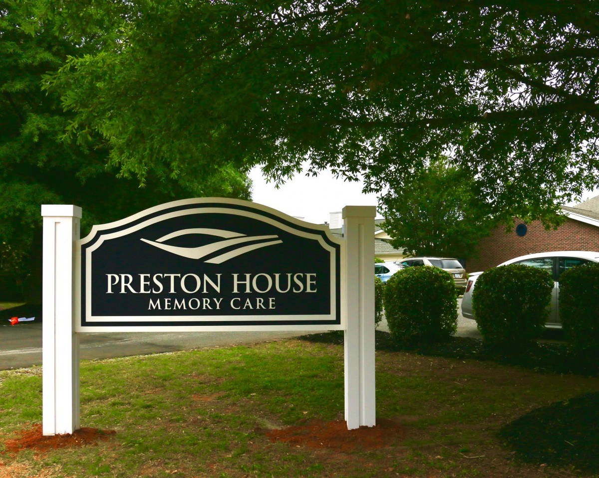 A sign for Preston House Memory Care surrounded by greenery.