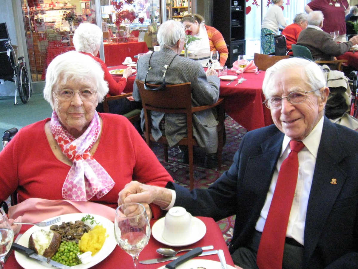 An elderly couple holding hands while dining at a restaurant.