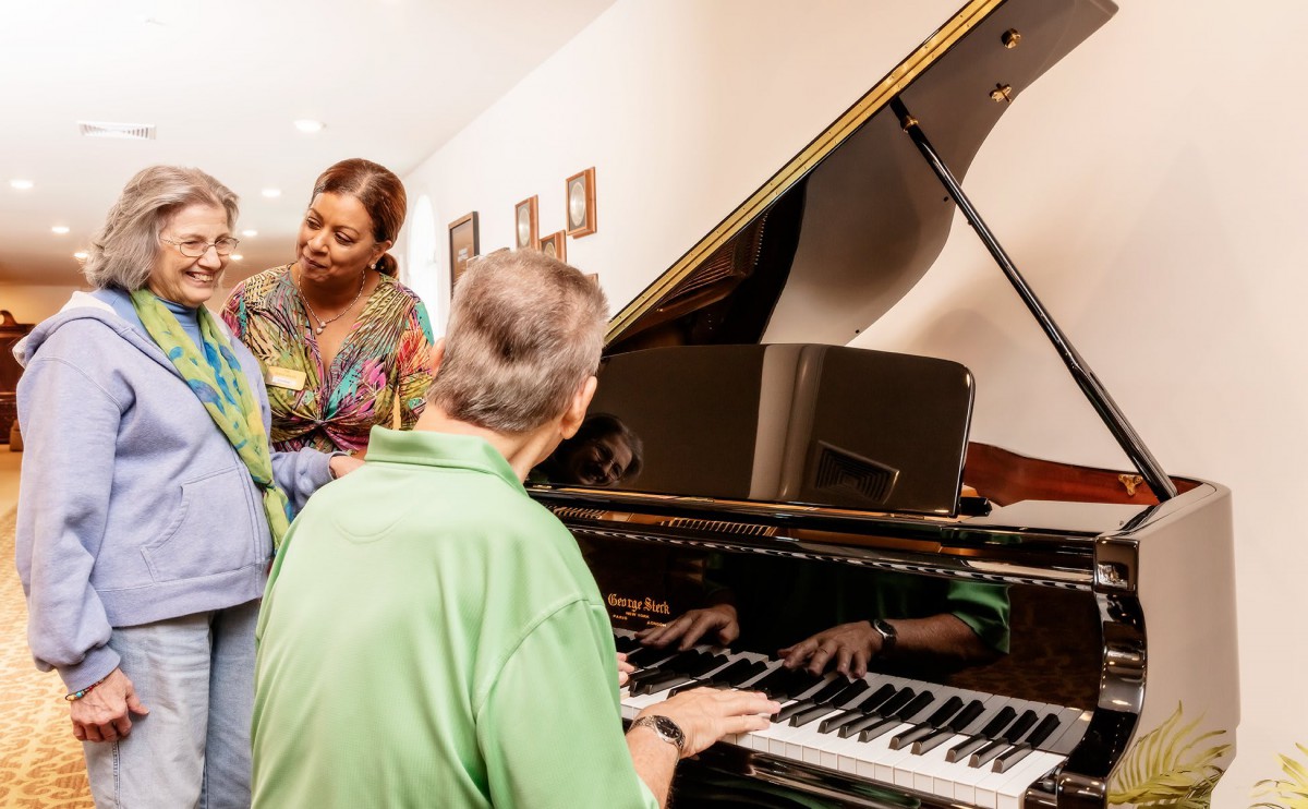 A group of people gathered around a grand piano, engaging in a musical moment.