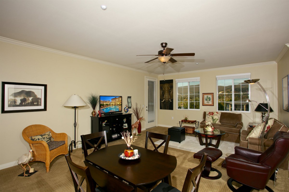 A cozy living room with a dining area, featuring comfortable seating, a television, and large windows.
