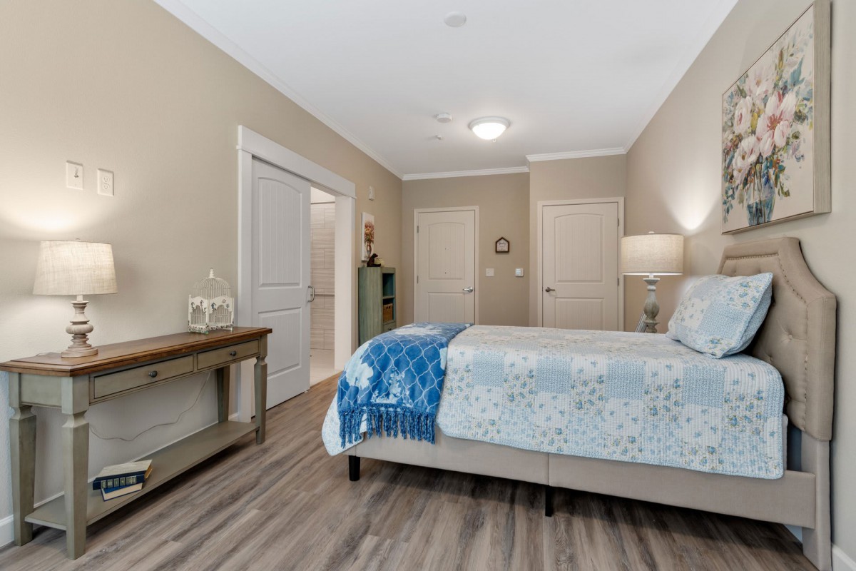 A modern bedroom with a neatly made bed, hardwood flooring, and subtle neutral decor.
