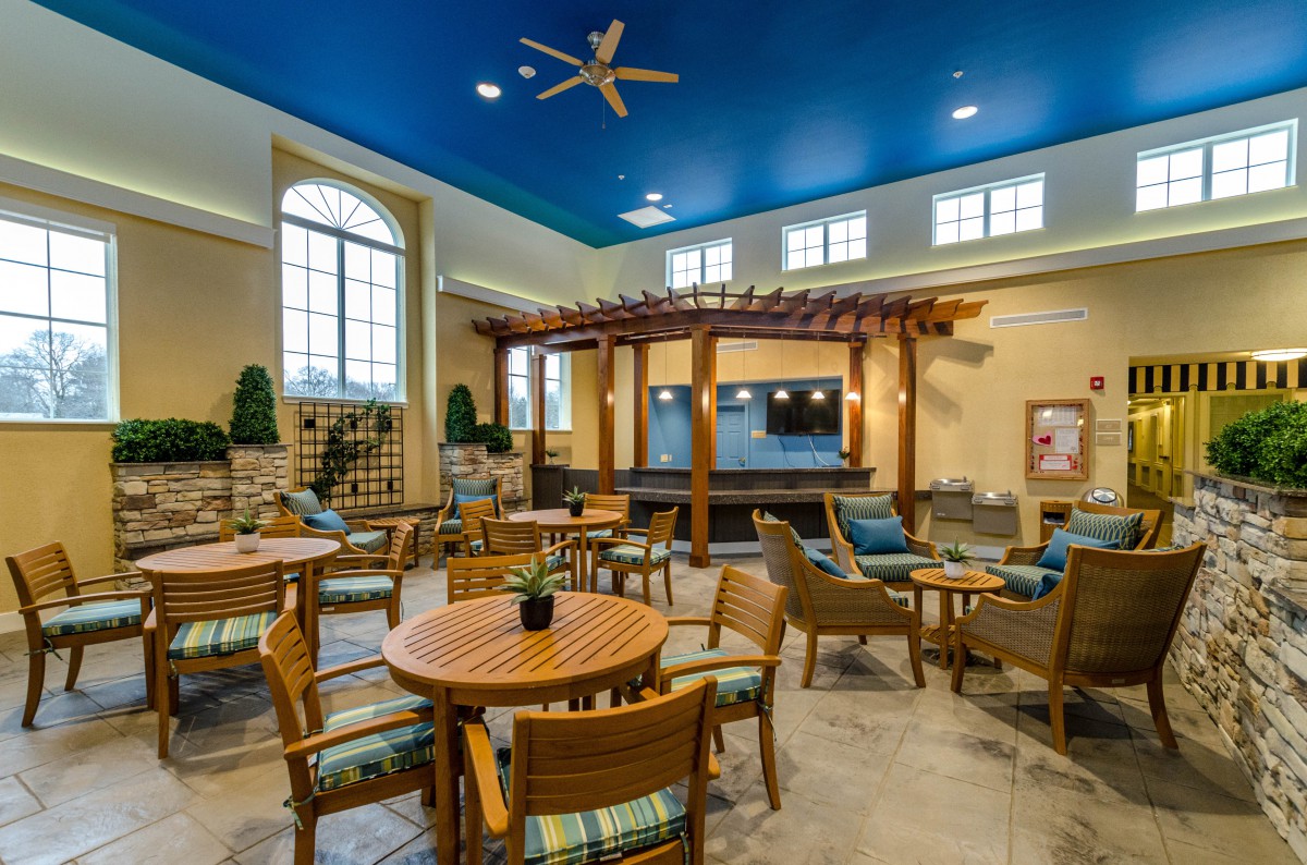 A cozy lounge area with wooden tables and chairs, featuring a blue ceiling and large windows.