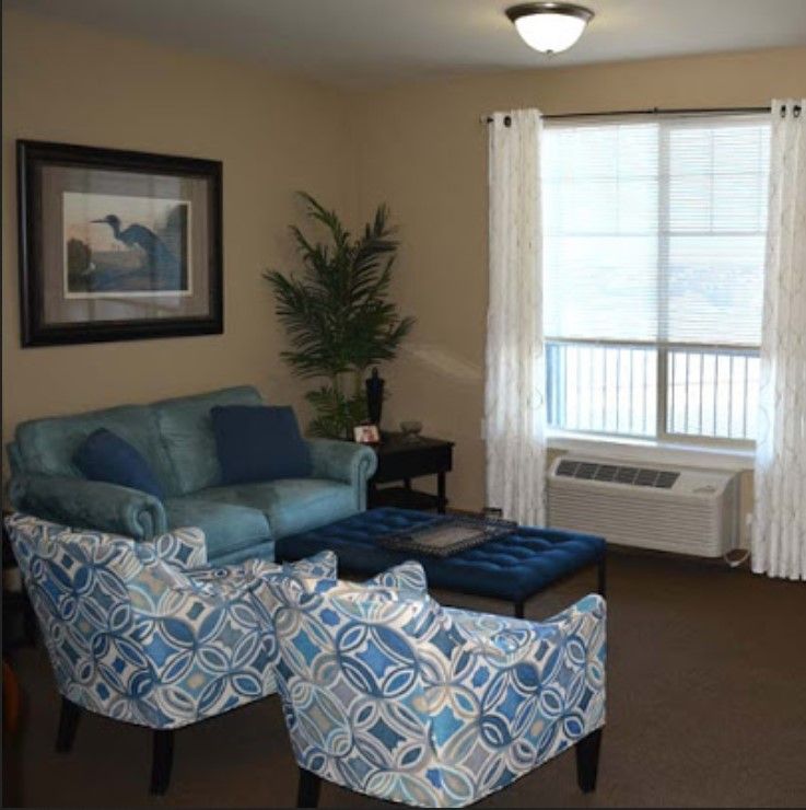 A cozy living room with a blue sofa and patterned armchairs, complemented by a coffee table and large window with white curtains.