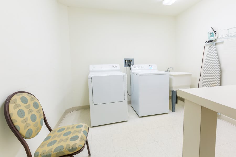 A bright laundry room featuring a washing machine, dryer, and a chair.