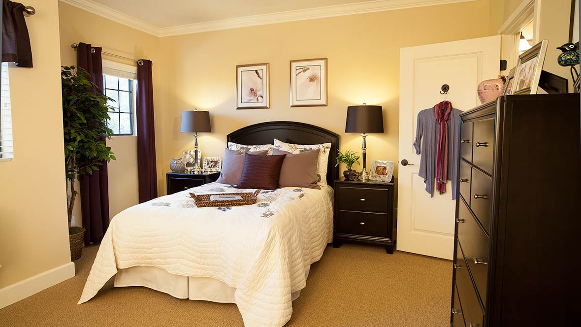 A cozy bedroom with a neatly made bed, two bedside tables with lamps, and framed pictures on the wall.