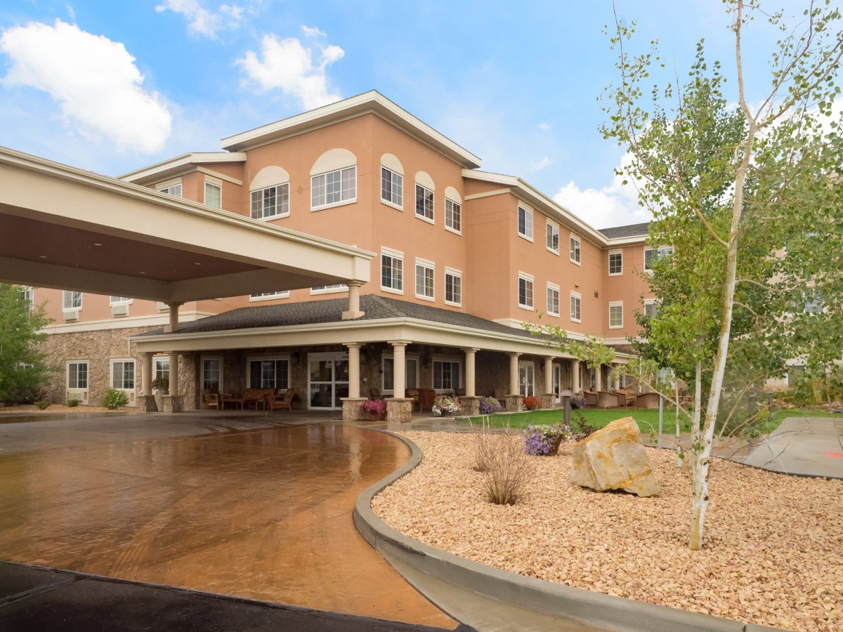 A modern multi-story building with a landscaped entrance and clear sky.