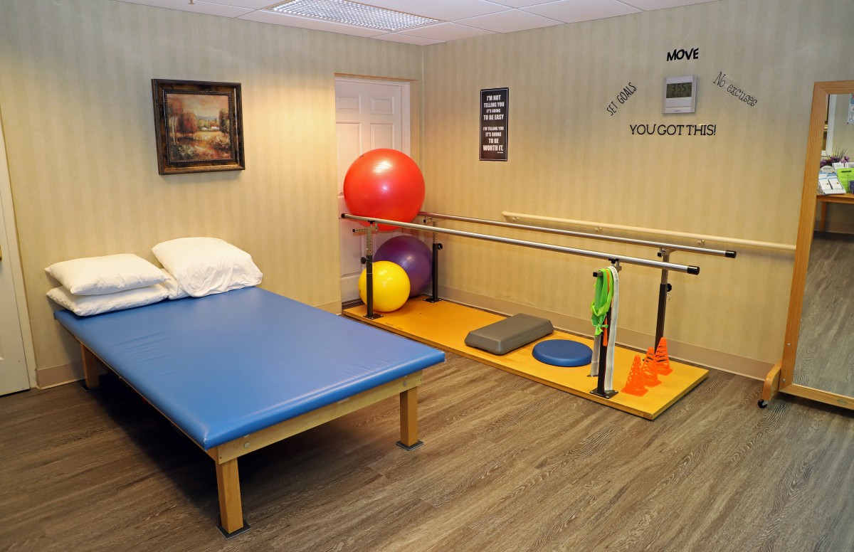 A physical therapy room equipped with a therapy table, exercise balls, and parallel bars.