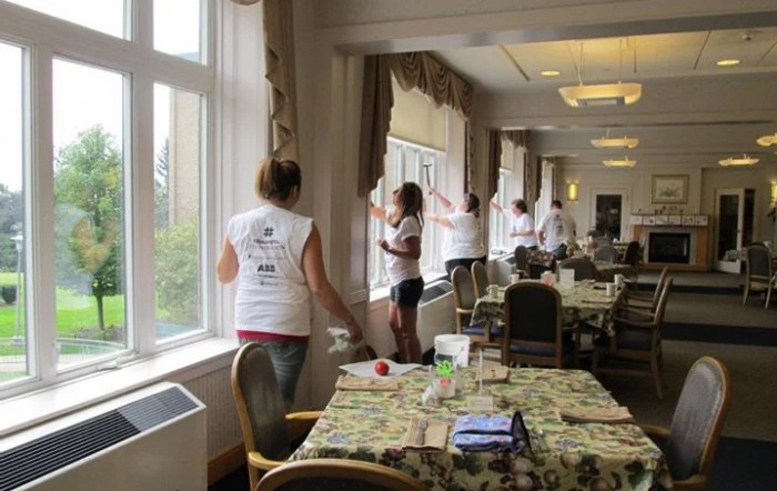 A group of volunteers cleaning windows in a community room.
