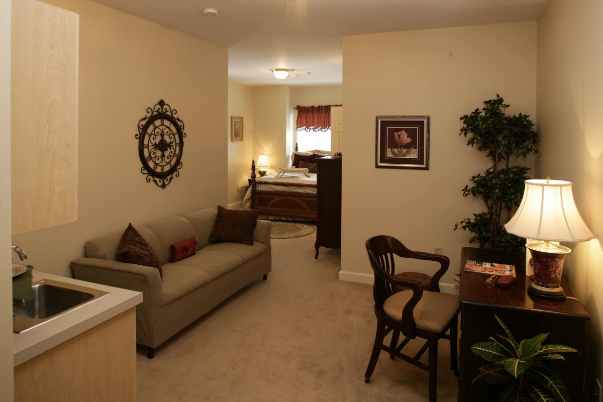 A cozy interior featuring a small living area with a sofa and chair, leading into a bedroom.