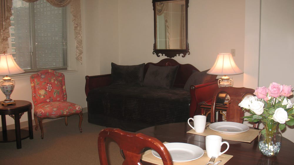 A cozy living room with a sofa, mirror, dining table set with cups, and a lamp.