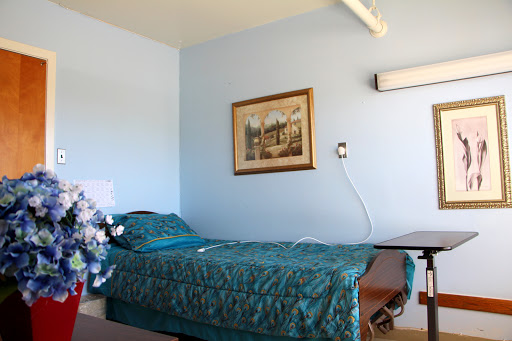 A hospital room featuring a single bed with a teal blanket and a piece of artwork on the wall.
