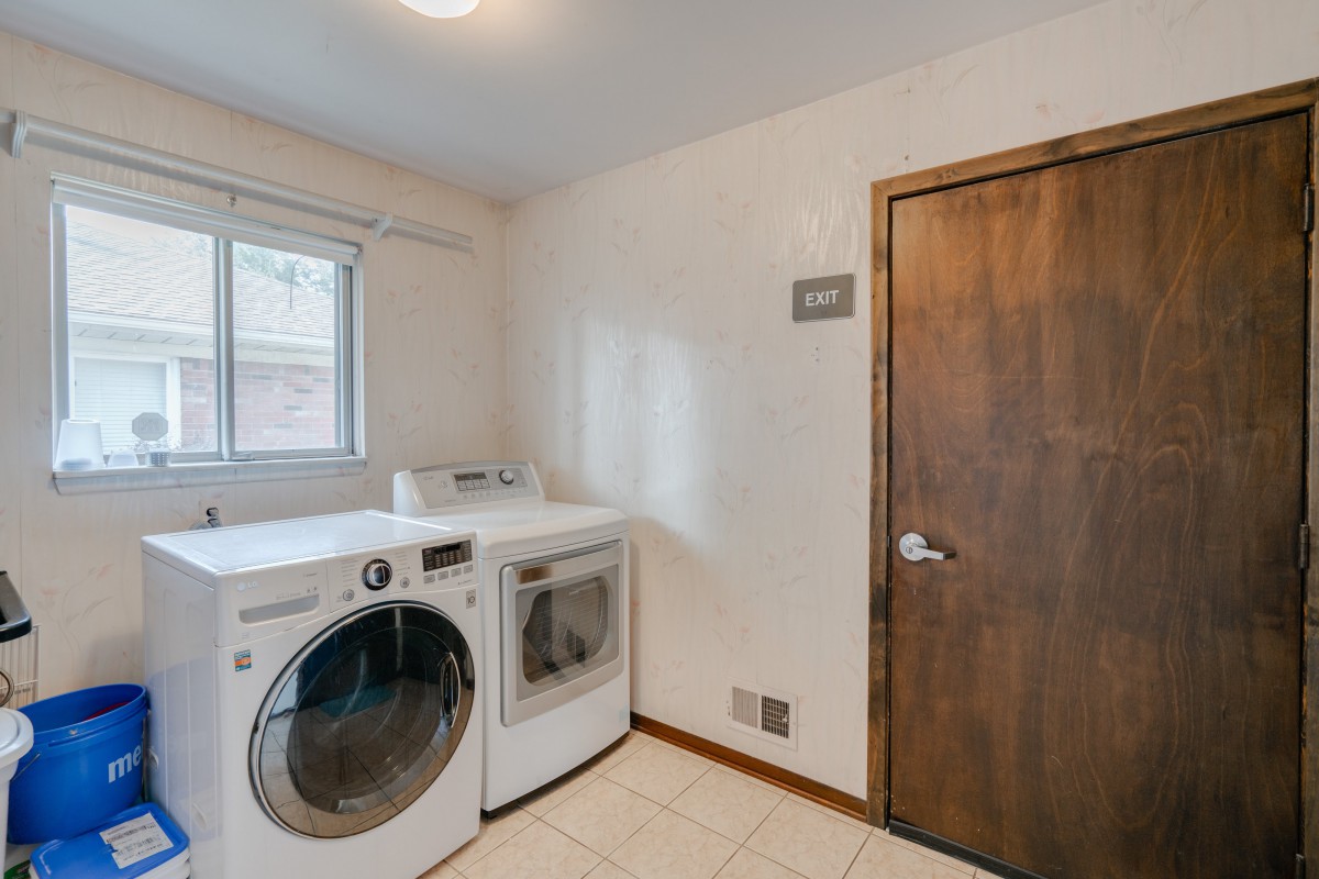 A laundry room featuring a washing machine and dryer positioned next to each other, with a window and a wooden door visible.