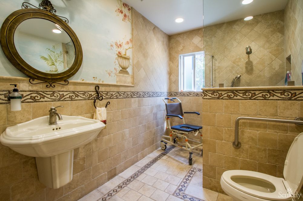 An accessible bathroom featuring a wheelchair, tiled walls, a sink, and a toilet.
