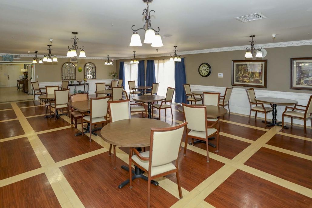 A spacious dining area with wooden floors, round tables, and elegant chandeliers.