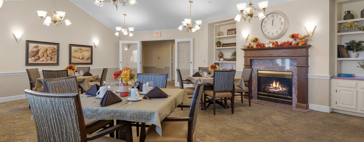A cozy dining room with neatly arranged tables and chairs, adorned with elegant chandeliers.