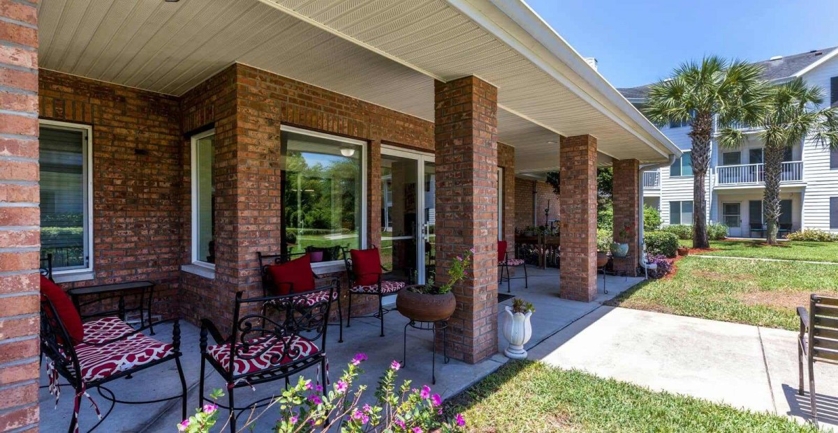 A cozy porch with brick walls, outdoor furniture, and garden views.