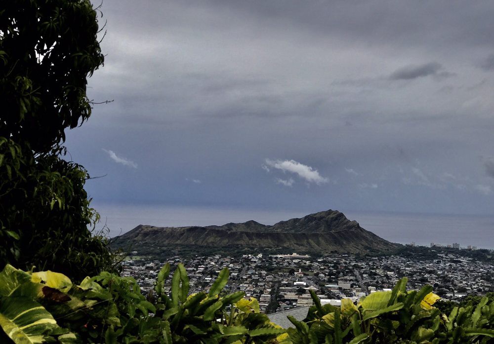 A scenic view of a city with mountains in the background under a cloudy sky.