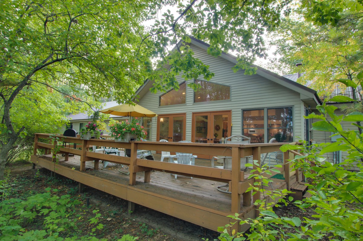 A cozy house surrounded by trees, featuring a wooden deck with outdoor seating.