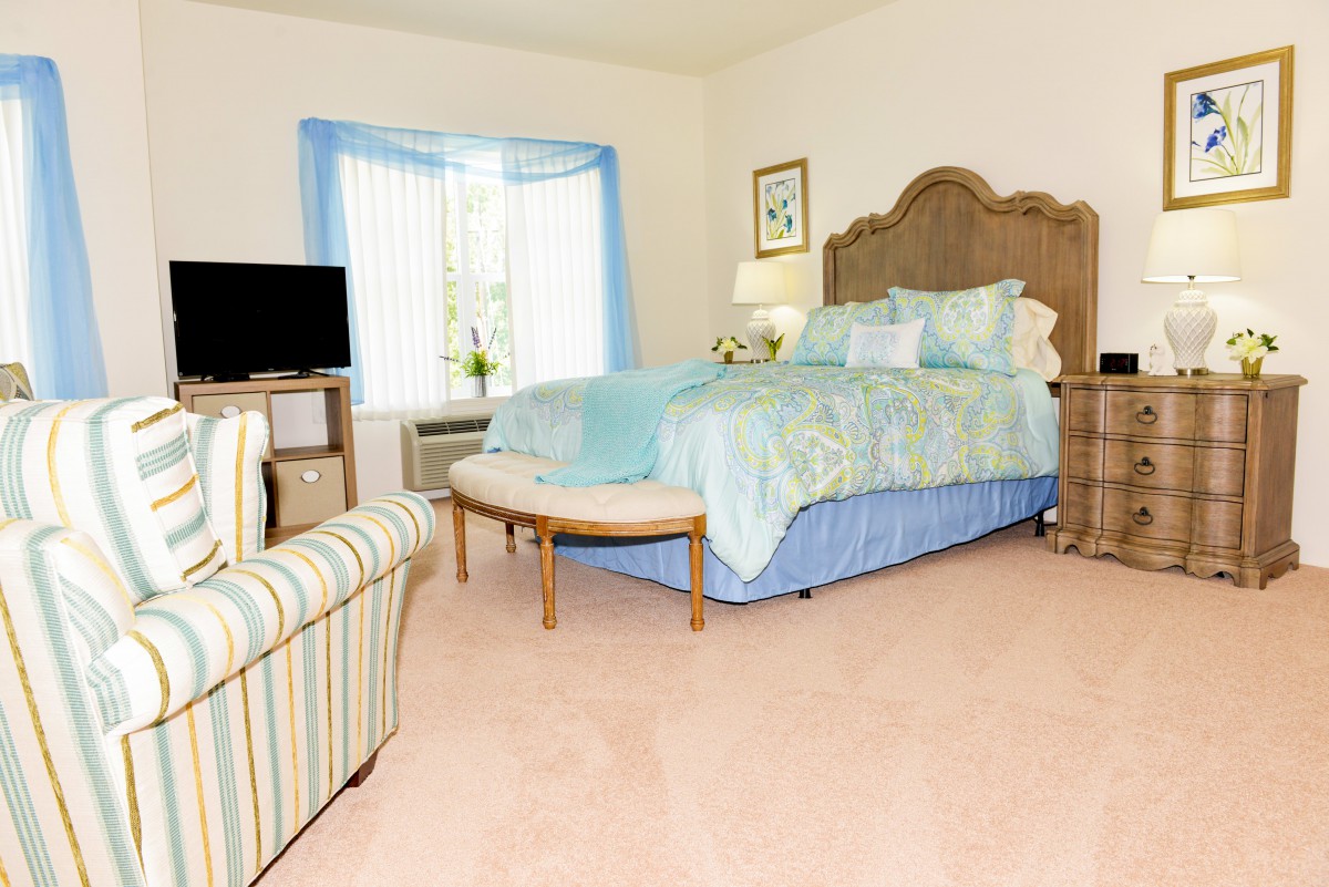 A cozy bedroom with blue accents, featuring a bed, television, and a large window.