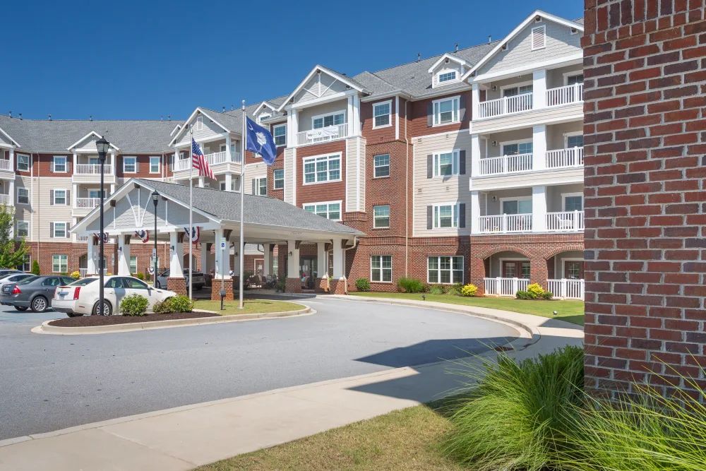 A multi-story residential building with balconies and flags at the entrance on a clear, sunny day.