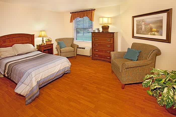 A cozy bedroom with a bed, armchairs, dresser, and various decor elements.