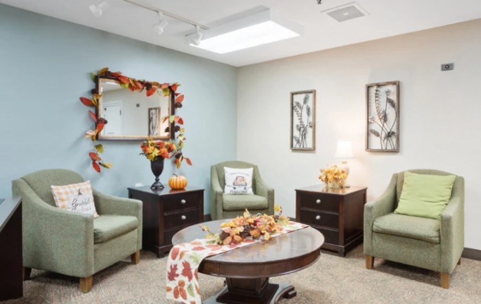 A cozy living room decorated with autumn-themed accessories, featuring armchairs, a coffee table, and wall art.