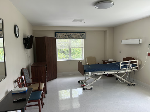 A bright and clean hospital patient room featuring a bed, furniture, and a window.
