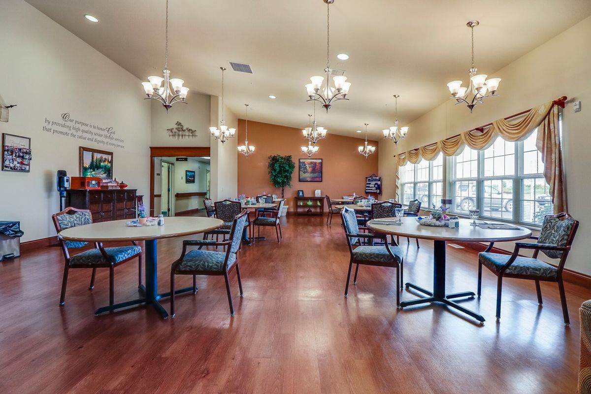 A spacious dining room with elegant chandeliers, multiple tables and chairs, featuring wood flooring and large windows.