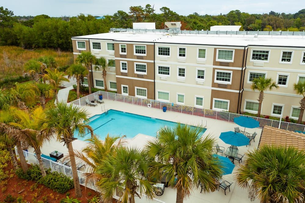Aerial view of an apartment complex with a swimming pool surrounded by palm trees.