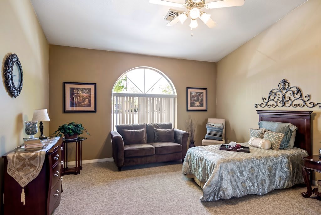 A cozy bedroom with a bed, sofa, and window letting in natural light.