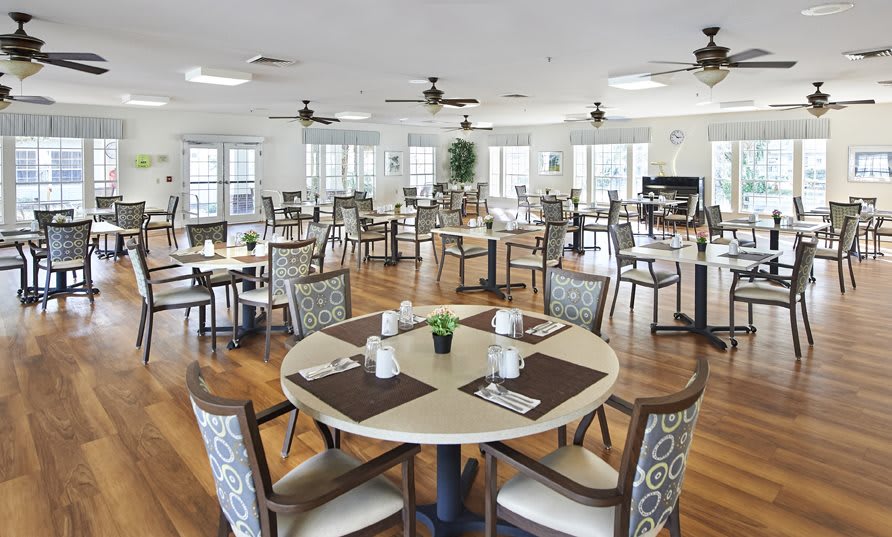 A spacious and elegantly designed dining area with multiple tables and chairs, featuring wooden flooring and large windows.