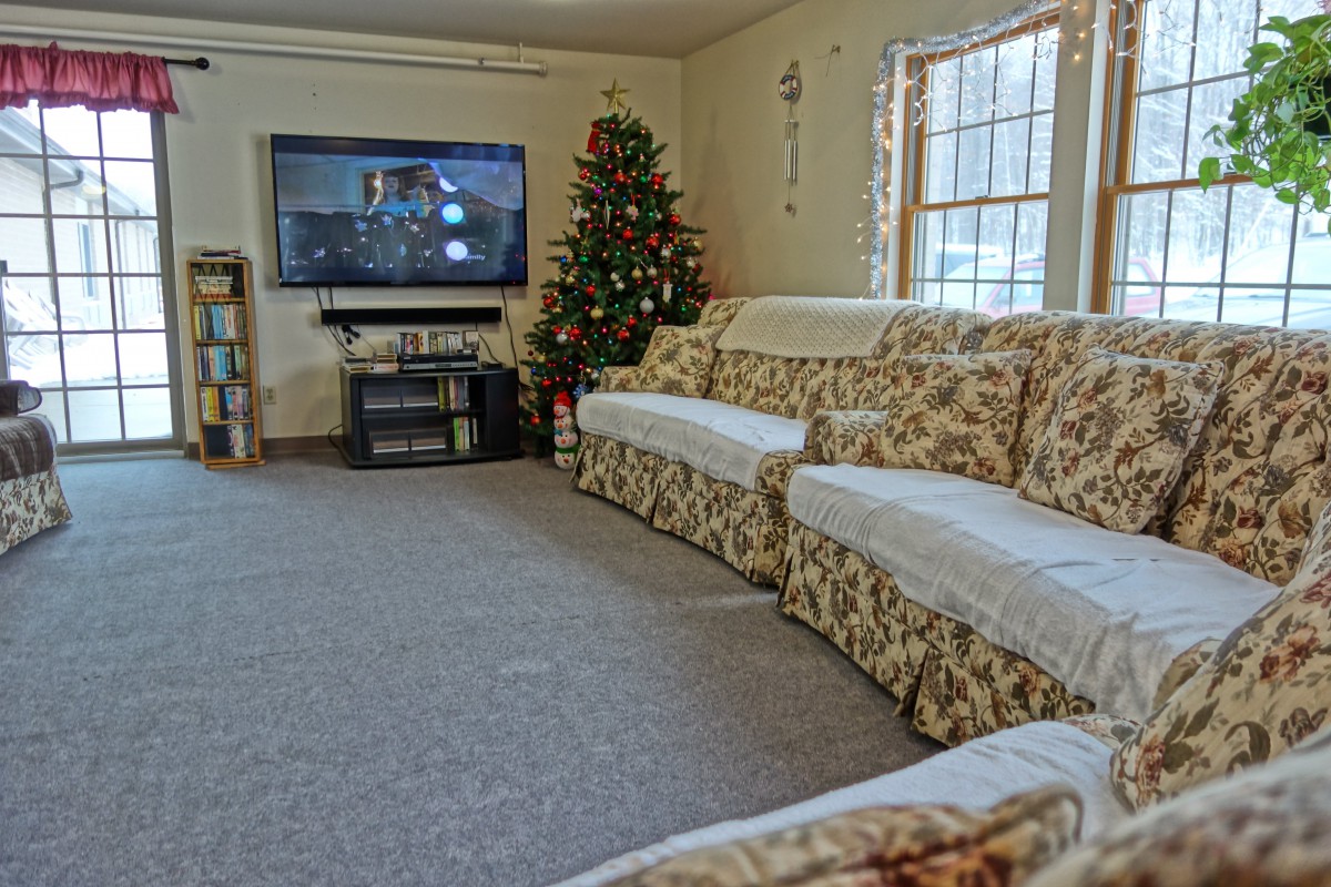 Cozy living room with a floral sofa and a festive Christmas tree, facing a mounted television.