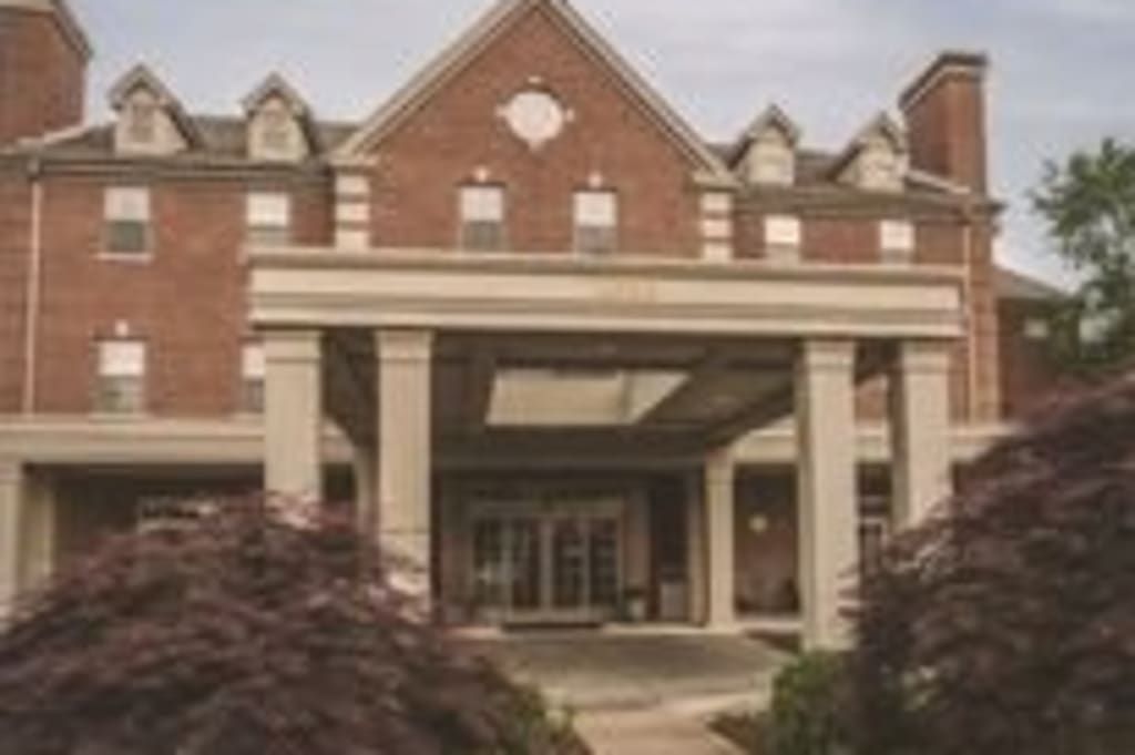 A brick building with a large entrance and columns, surrounded by trees.