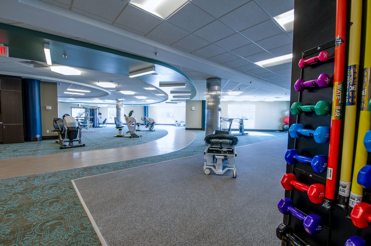 A spacious gym with various exercise equipment and a rack of colorful weights.