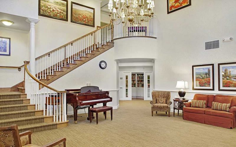 A spacious foyer with a grand staircase, a piano, and elegant furnishings.