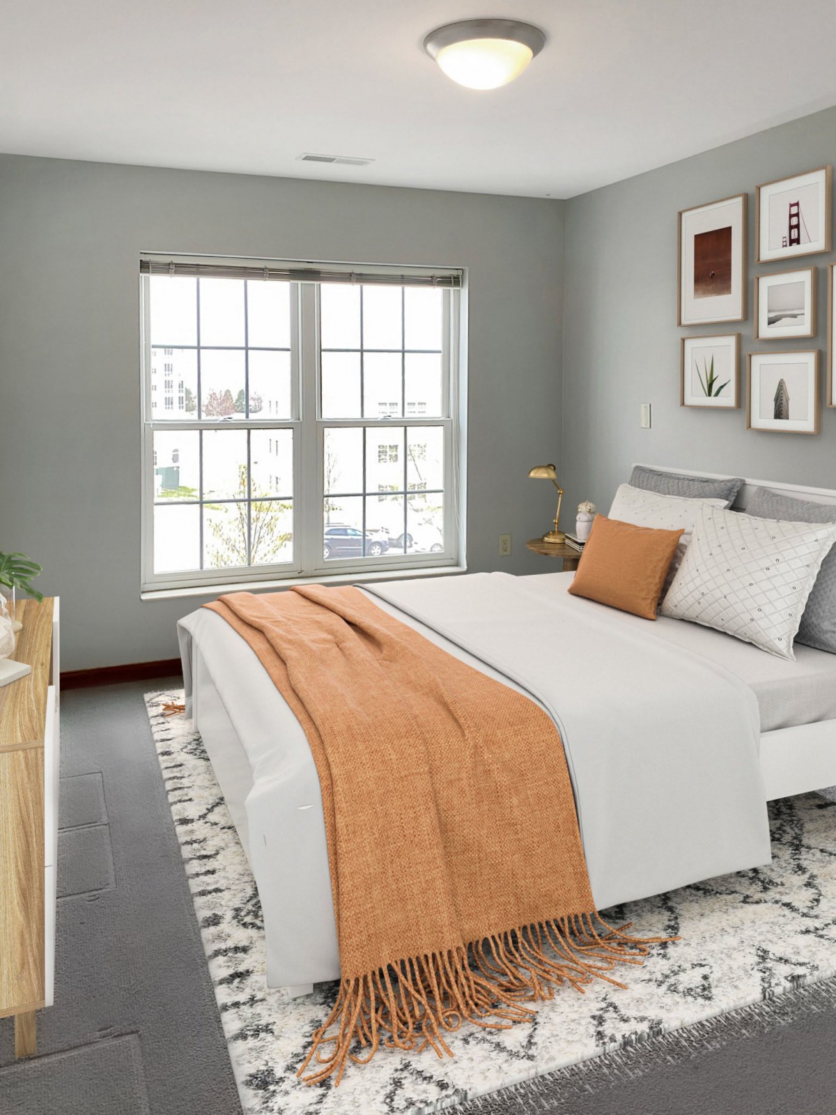 A modern and minimalist bedroom with a cozy orange accent blanket and ample natural light.